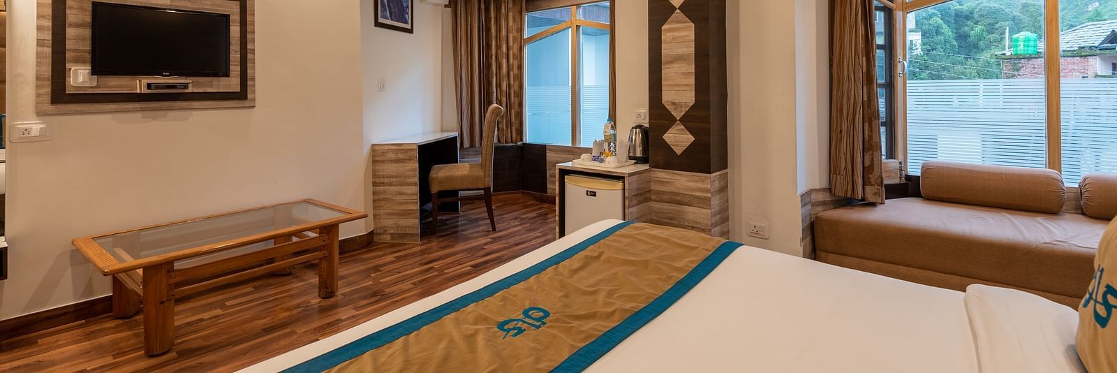 A spacious hotel room with a large bed, a TV, a desk, and a window with a view - DLS Meghavan Resort